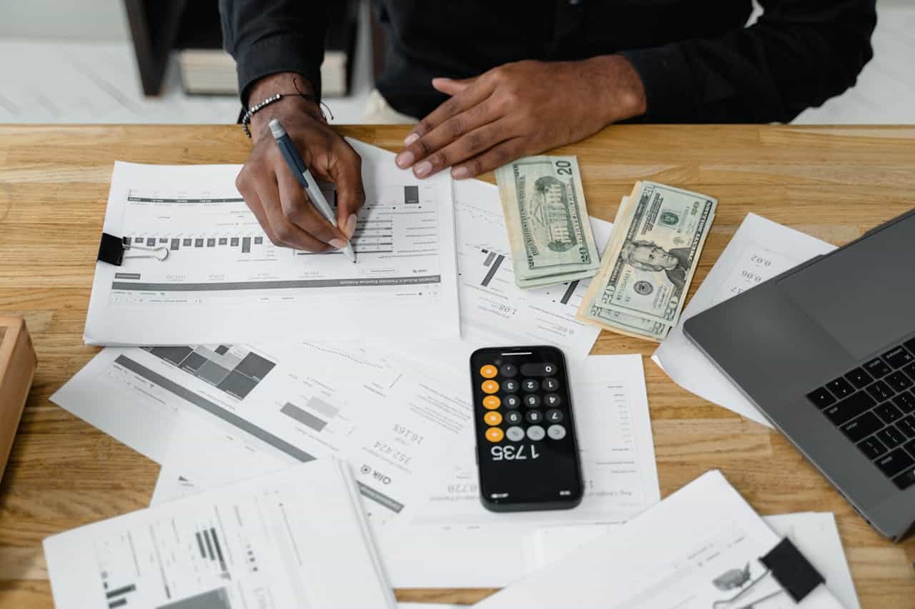 Services Man working on financial reports with calculator, money, and laptop on a desk.
