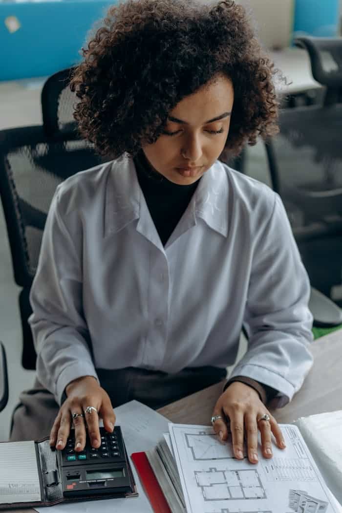 Contact Businesswoman calculating finances at her desk with documents and a calculator.